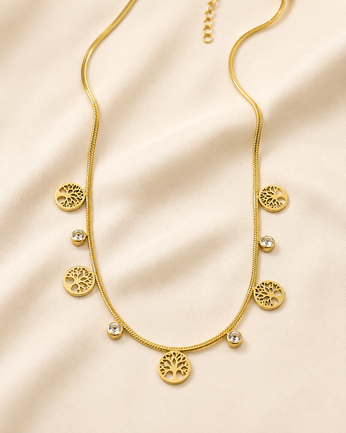 Collar dorado con dijes de árbol de la vida y zirconias sobre satén color hueso