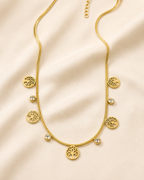 Collar dorado con dijes de árbol de la vida y zirconias sobre satén color hueso