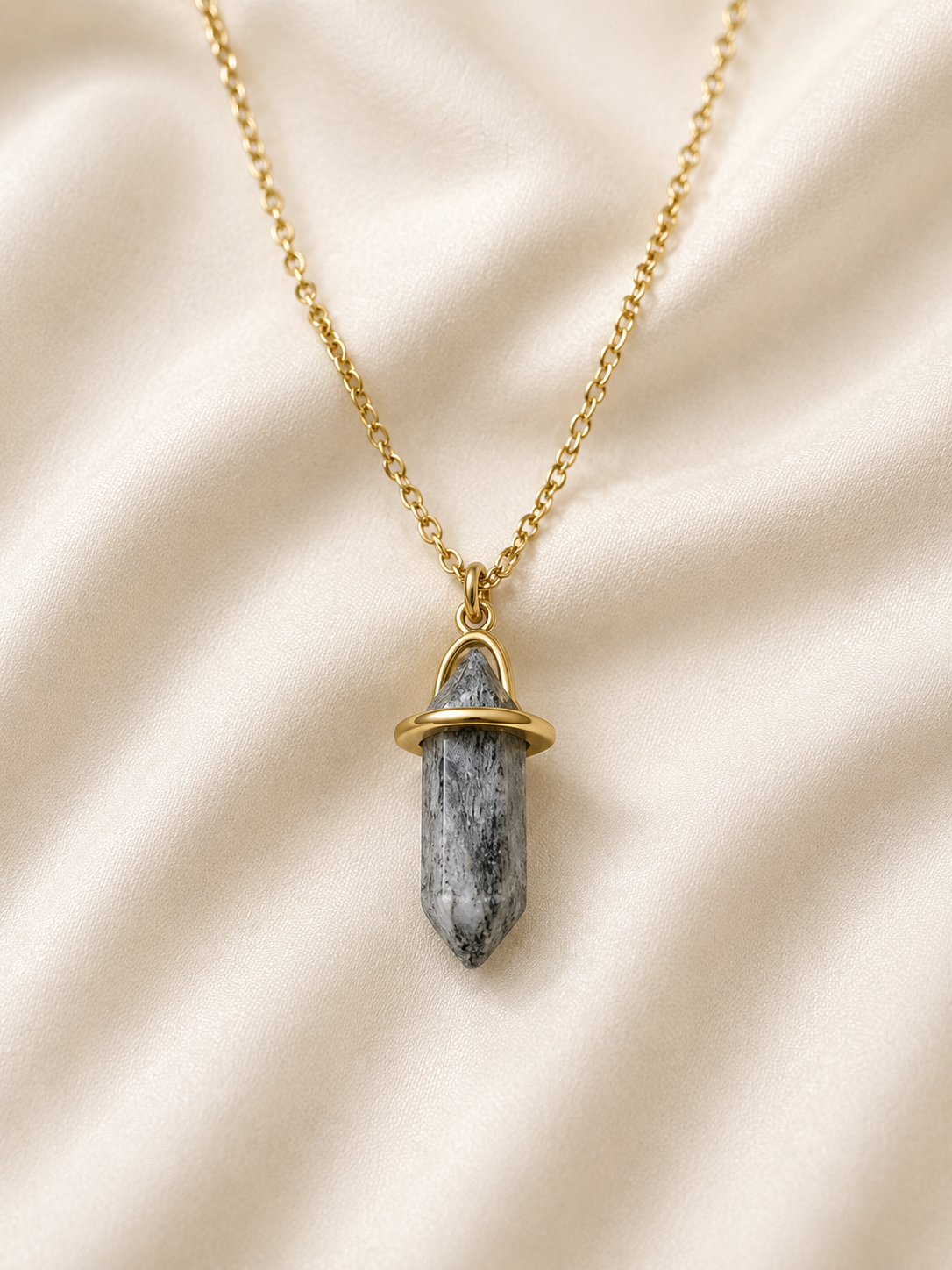 Collar dorado con piedra natural tallada en punta sobre satén color hueso