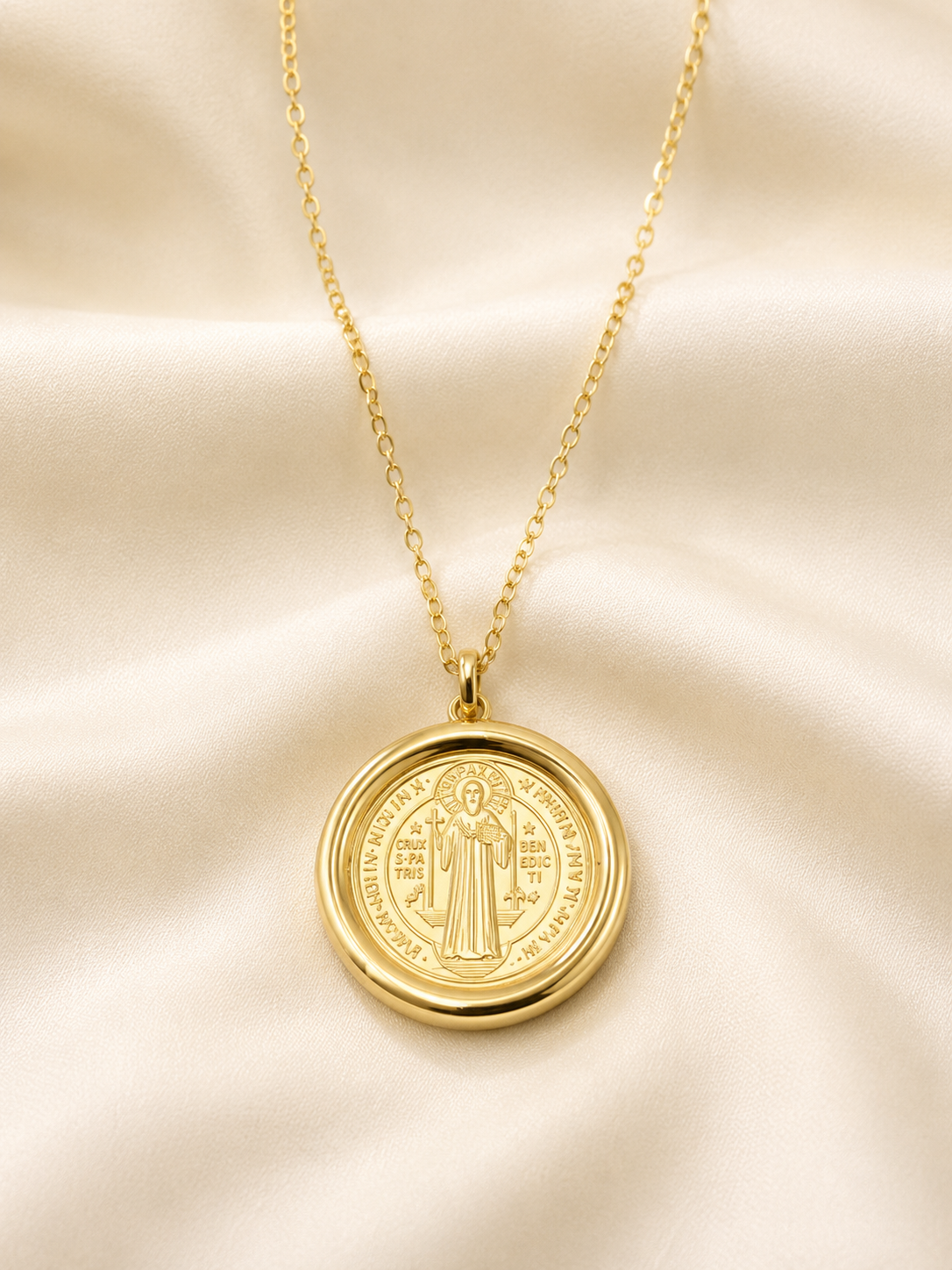 Collar dorado con medalla de san Benito sobre satén color hueso