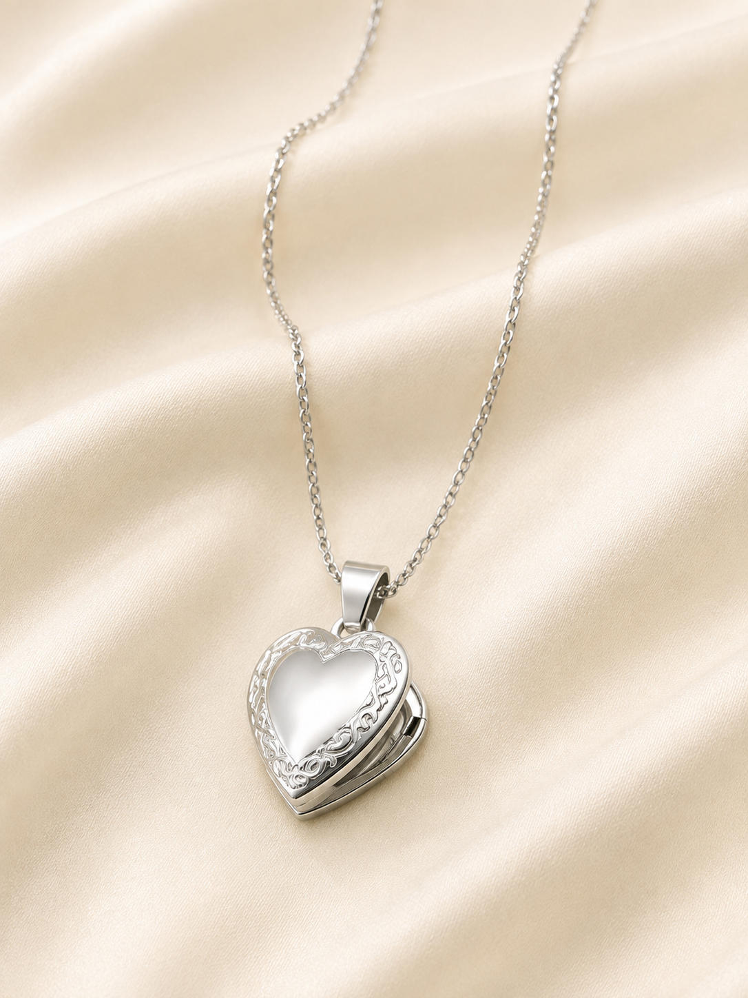 Collar plateado con relicario de corazón sobre satén color hueso